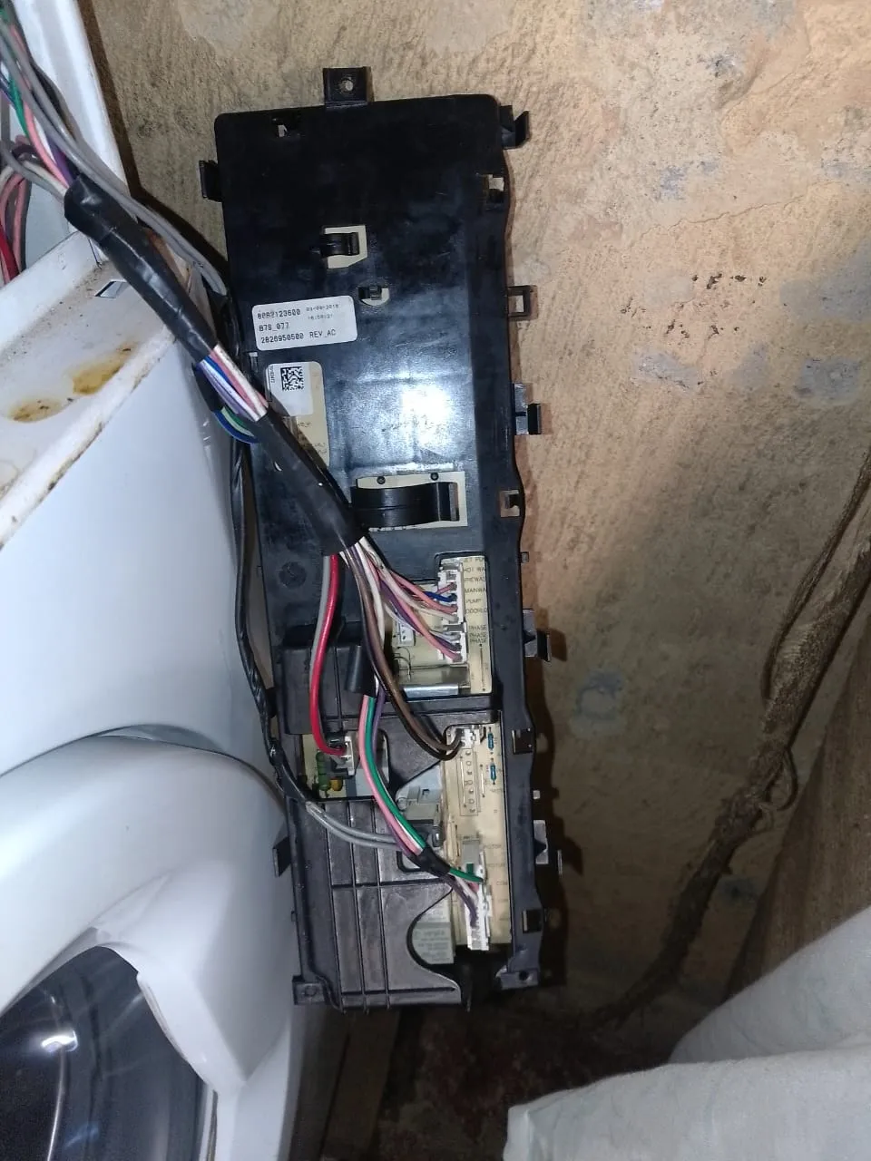 Washing machine control board removed from the machine with the wiring loom still attached, showing the relays and circuitry that sit behind the front panel