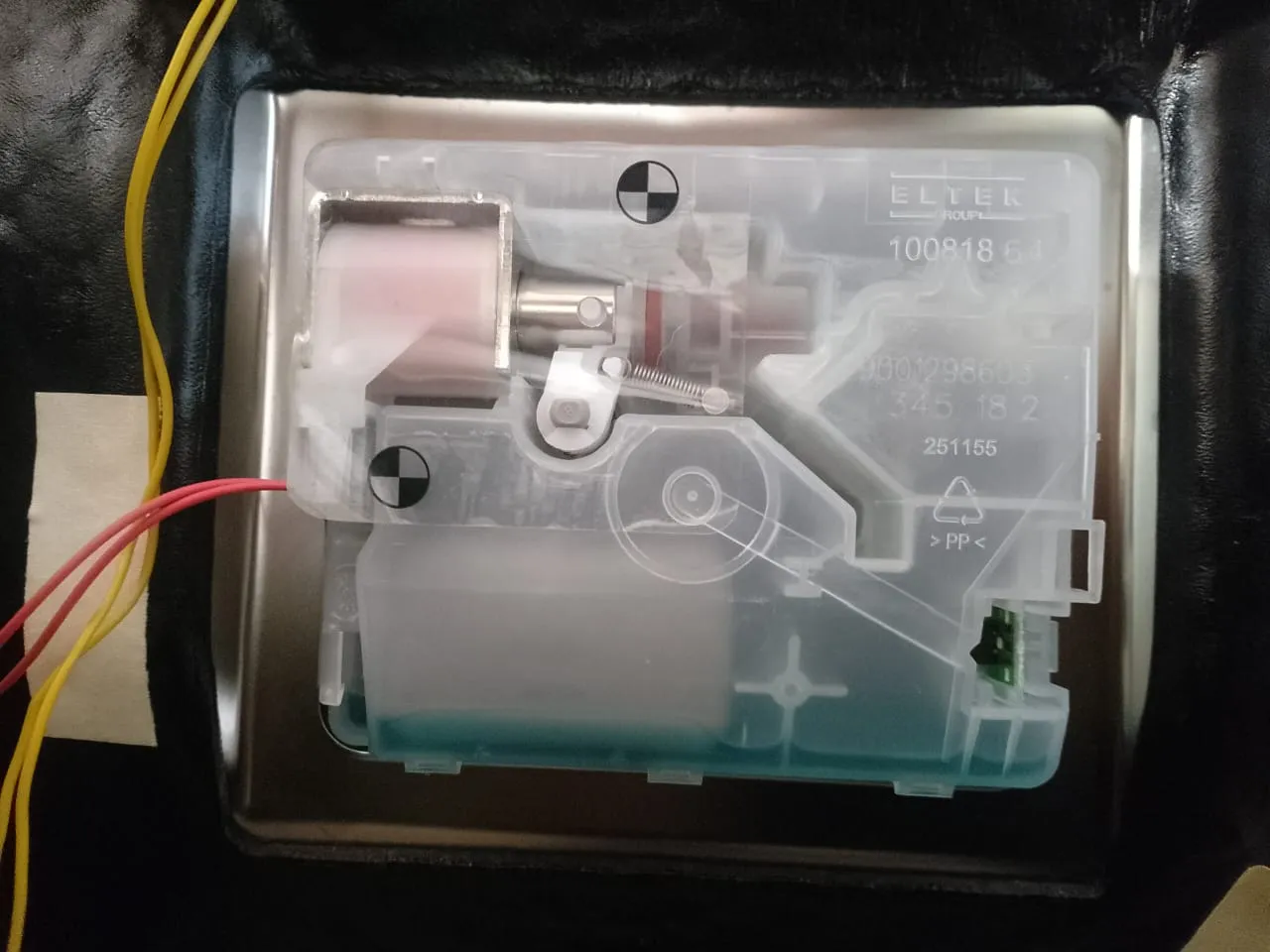 Back of a Bosch dishwasher soap dispenser inside the door, showing the electric release coil, latch spring and wiring