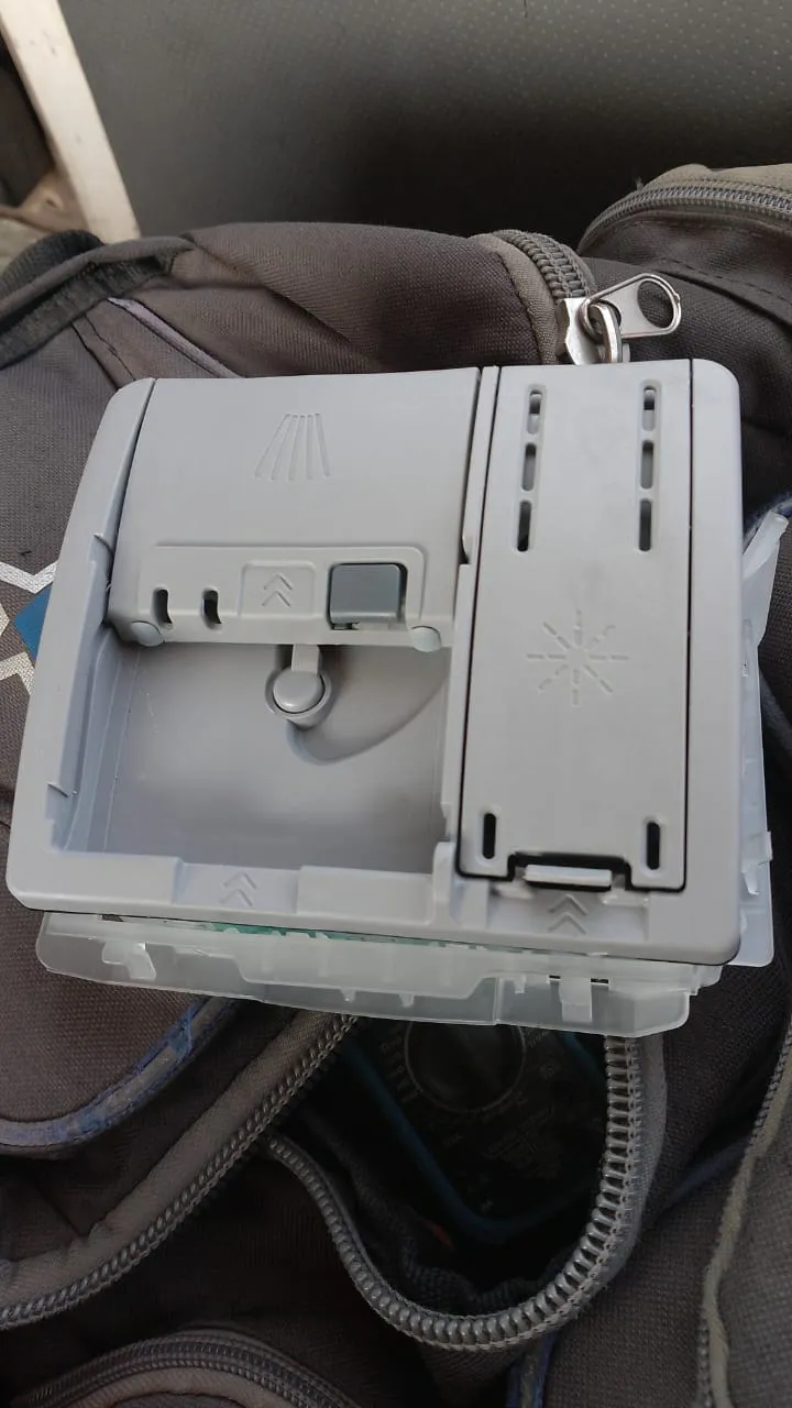 Bosch dishwasher soap dispenser removed from the door, showing the detergent cup, release catch and rinse-aid compartment